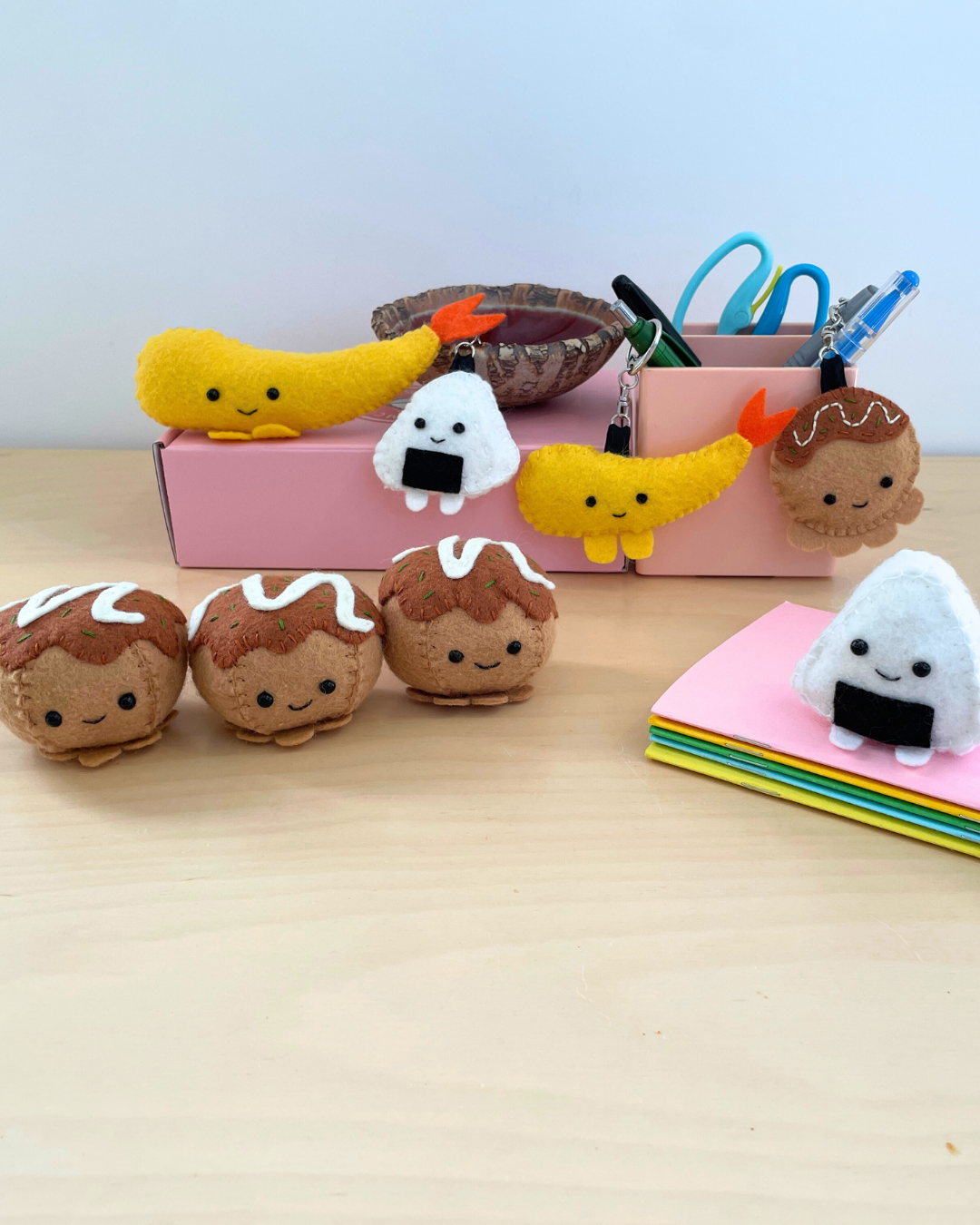 Felt plush toys resembling Japanese takoyaki, onigiri, and shrimp tempura on a wooden surface with a light blue background